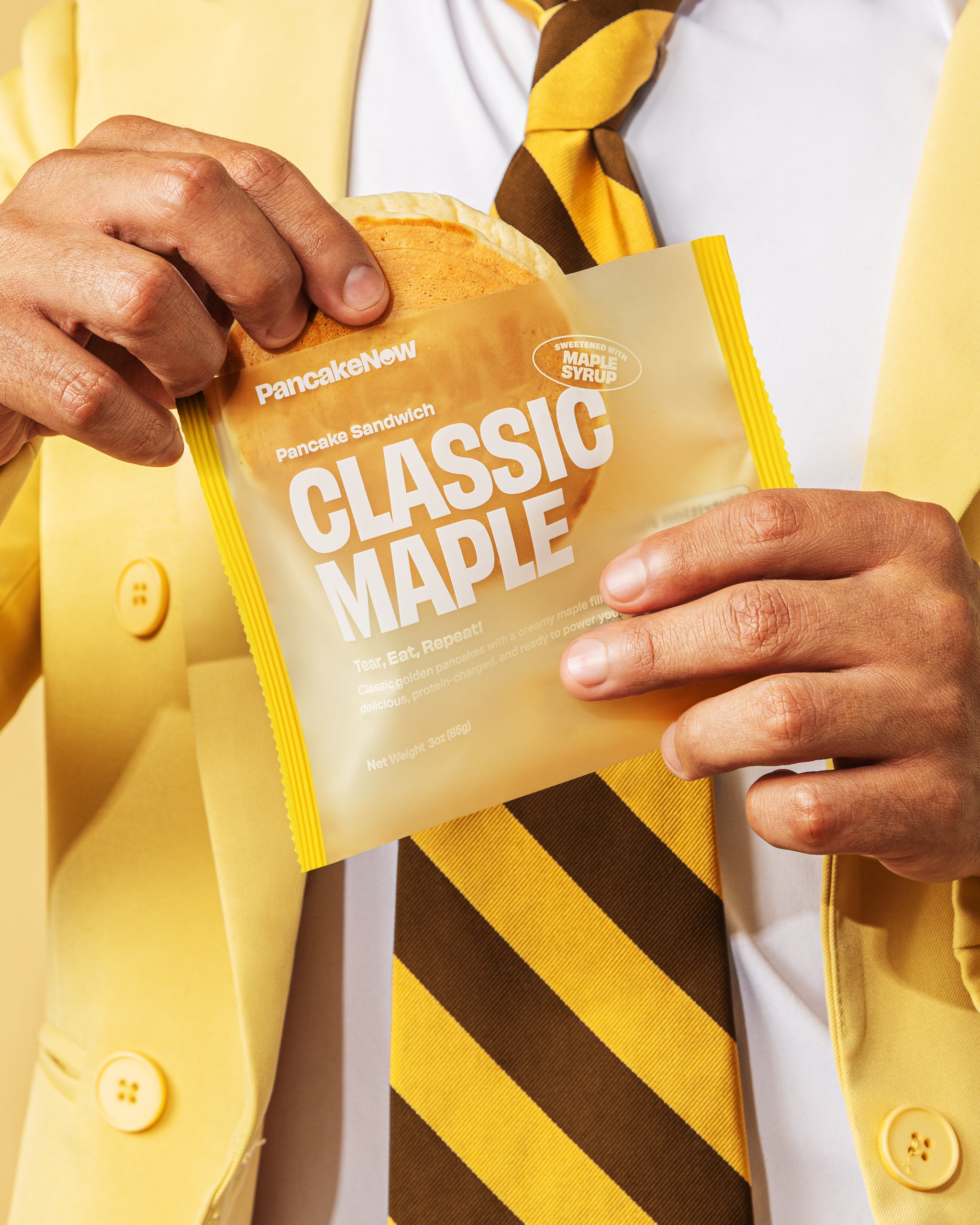 Person holding a Classic Maple Pancake Sandwich package with a yellow jacket and striped tie.